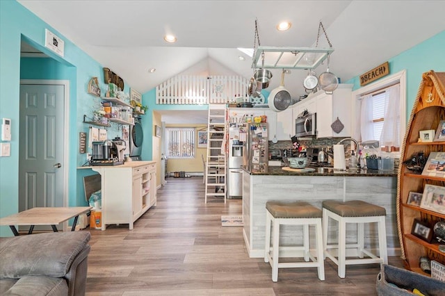 kitchen featuring light wood-type flooring, a kitchen bar, white cabinetry, appliances with stainless steel finishes, and vaulted ceiling