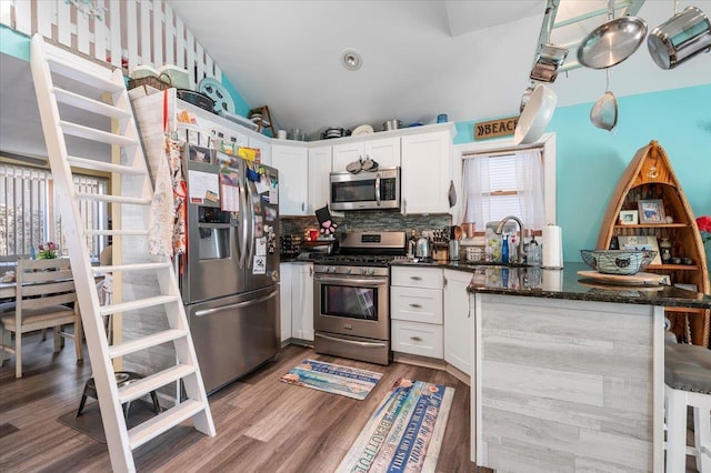 kitchen with a sink, wood finished floors, stainless steel appliances, a peninsula, and white cabinets