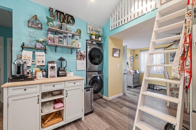 laundry area with laundry area, baseboards, stacked washer / drying machine, and light wood-style floors