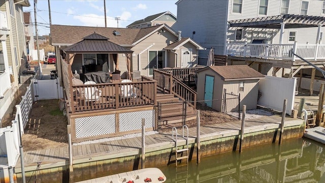 rear view of house featuring a storage unit, a pergola, a fenced backyard, an outdoor structure, and a deck with water view