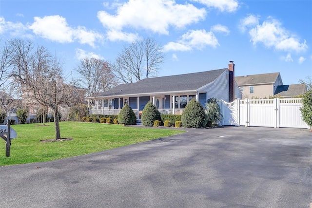 ranch-style home featuring driveway, a gate, fence, covered porch, and a front yard