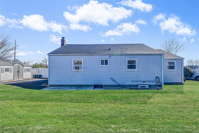 rear view of property with an outbuilding, a lawn, a storage shed, and fence