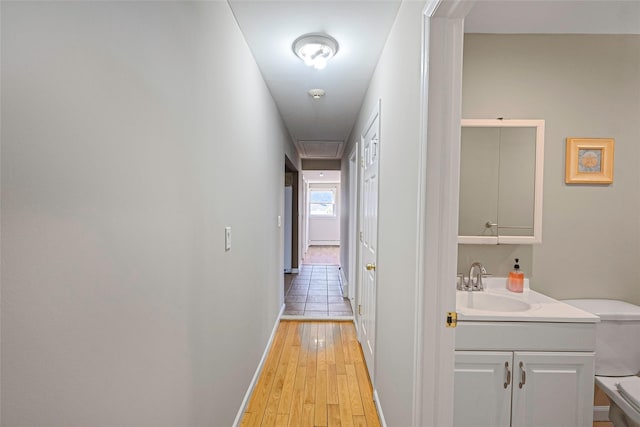 hall with light wood finished floors, baseboards, and a sink