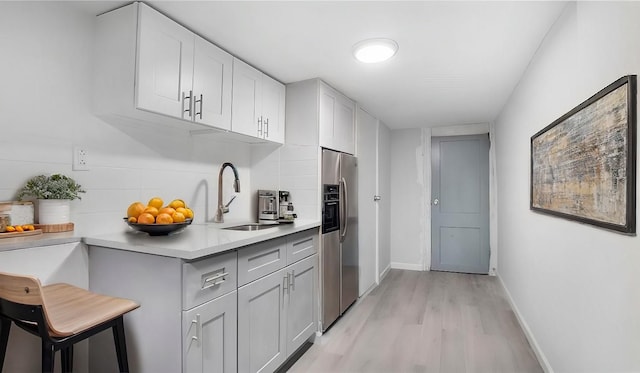 kitchen featuring stainless steel refrigerator with ice dispenser, a sink, backsplash, light wood-style floors, and light countertops