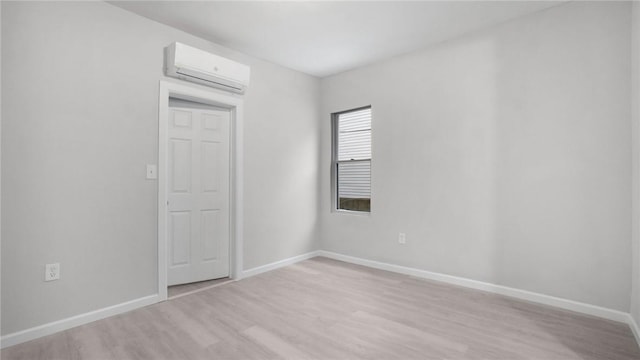 empty room featuring baseboards, light wood-style flooring, and a wall mounted AC