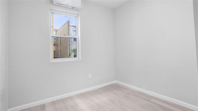 empty room featuring an AC wall unit, baseboards, and light wood-type flooring