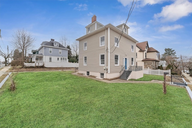 rear view of property with a lawn, a chimney, and fence