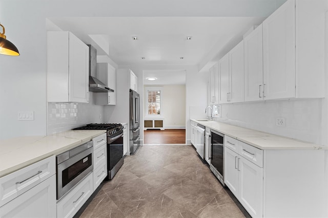 kitchen featuring a sink, wine cooler, white cabinets, appliances with stainless steel finishes, and wall chimney range hood