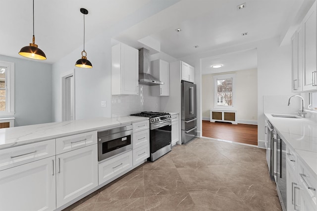 kitchen featuring a sink, light stone counters, stainless steel appliances, wall chimney range hood, and decorative backsplash