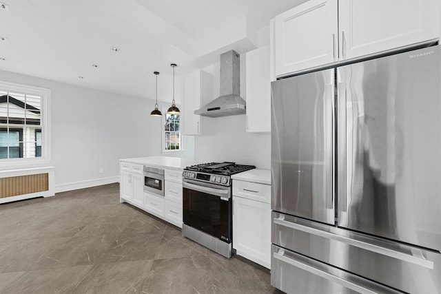 kitchen with radiator, light countertops, appliances with stainless steel finishes, white cabinetry, and wall chimney range hood