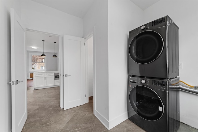 clothes washing area featuring laundry area, stacked washer / drying machine, and baseboards