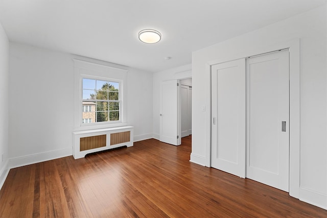 unfurnished bedroom featuring radiator, wood finished floors, baseboards, and a closet