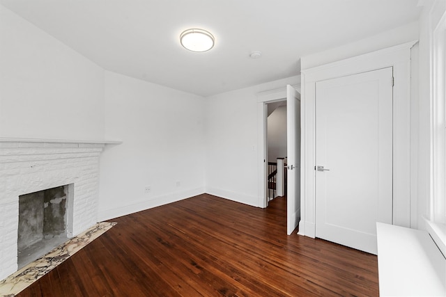 unfurnished living room with dark wood-style floors, a brick fireplace, and baseboards