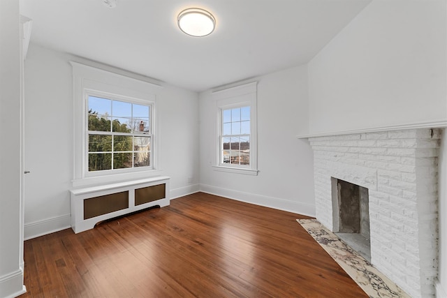 unfurnished living room featuring hardwood / wood-style flooring, a brick fireplace, and baseboards