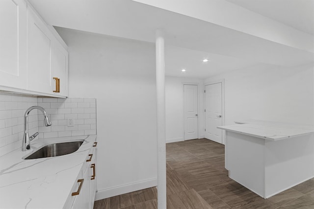 kitchen with a sink, light stone counters, backsplash, white cabinets, and baseboards