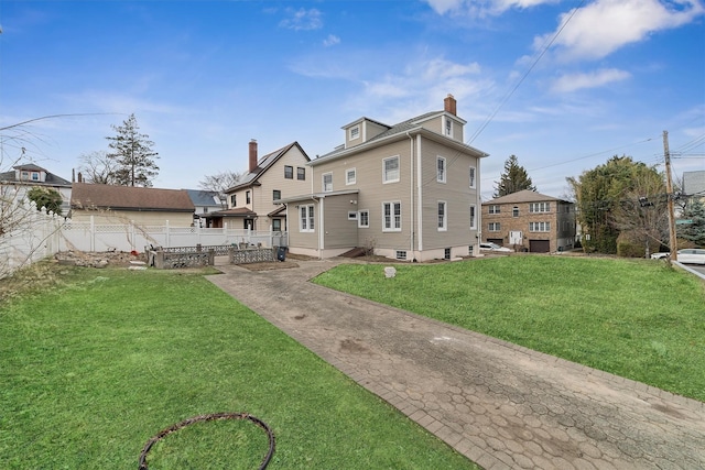 rear view of house featuring a lawn, fence, and a chimney