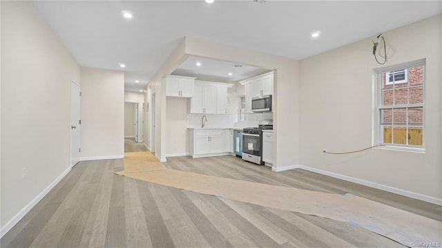 unfurnished living room featuring a sink, light wood-type flooring, baseboards, and recessed lighting