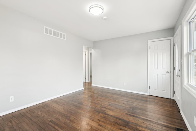 empty room featuring dark wood-type flooring, baseboards, and visible vents