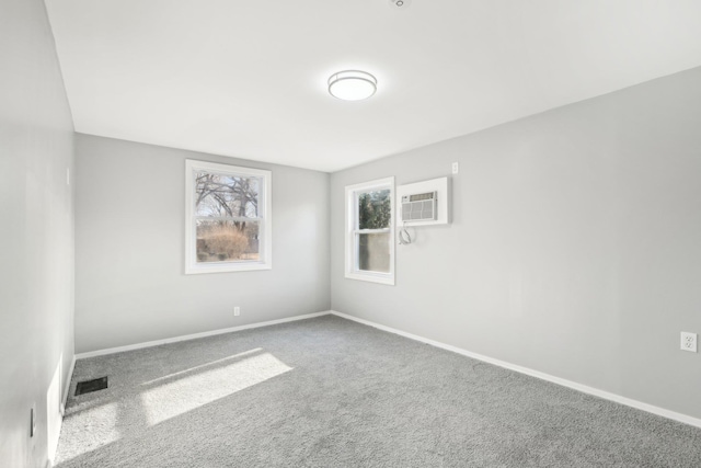 carpeted spare room featuring a wall unit AC, visible vents, and baseboards