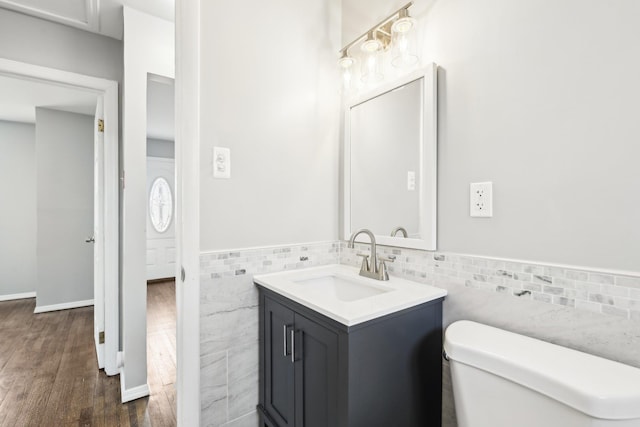 half bathroom featuring vanity, wood finished floors, a wainscoted wall, tile walls, and toilet