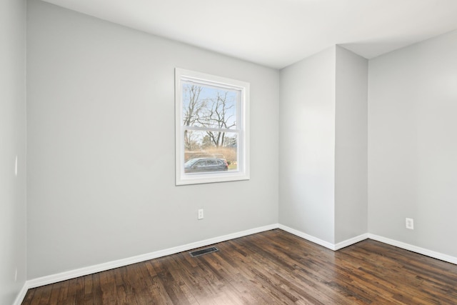 unfurnished room with dark wood-type flooring, visible vents, and baseboards