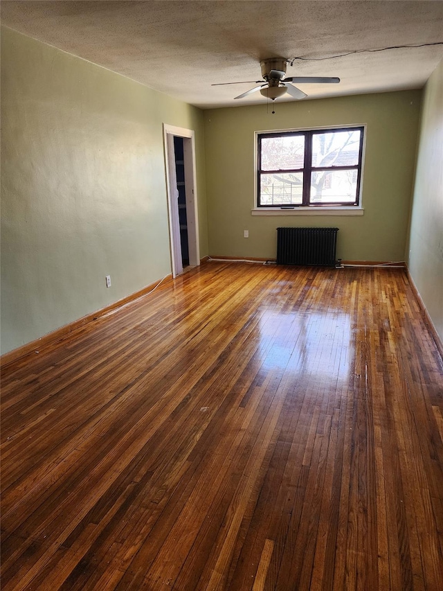 empty room with hardwood / wood-style flooring, a textured ceiling, radiator heating unit, baseboards, and ceiling fan