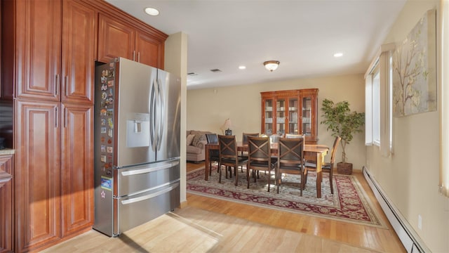 kitchen with brown cabinetry, light wood finished floors, recessed lighting, a baseboard heating unit, and stainless steel fridge