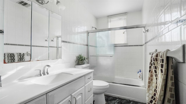 full bathroom with visible vents, bath / shower combo with glass door, toilet, vanity, and tile walls