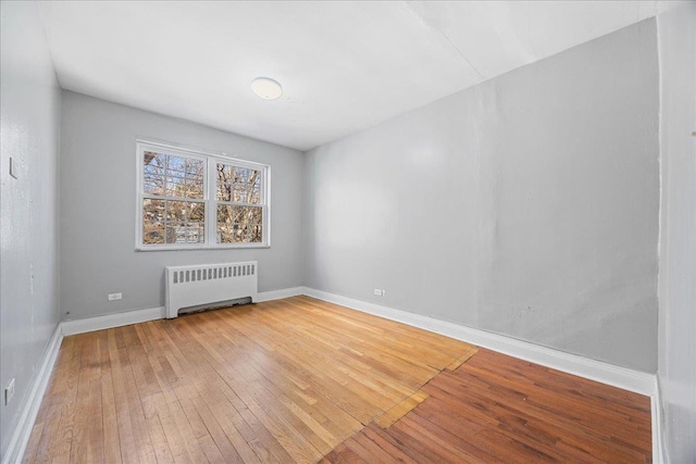 unfurnished room featuring hardwood / wood-style floors, radiator, and baseboards