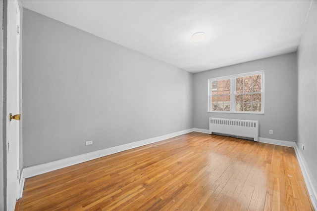 empty room featuring baseboards, radiator heating unit, and light wood-style floors