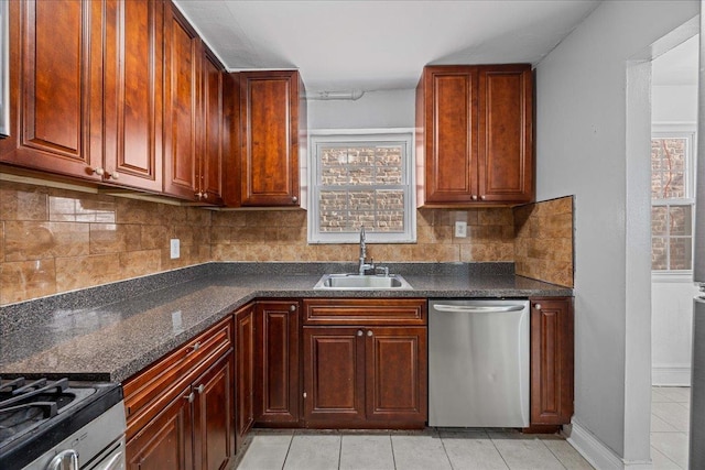 kitchen featuring dark countertops, backsplash, light tile patterned floors, appliances with stainless steel finishes, and a sink