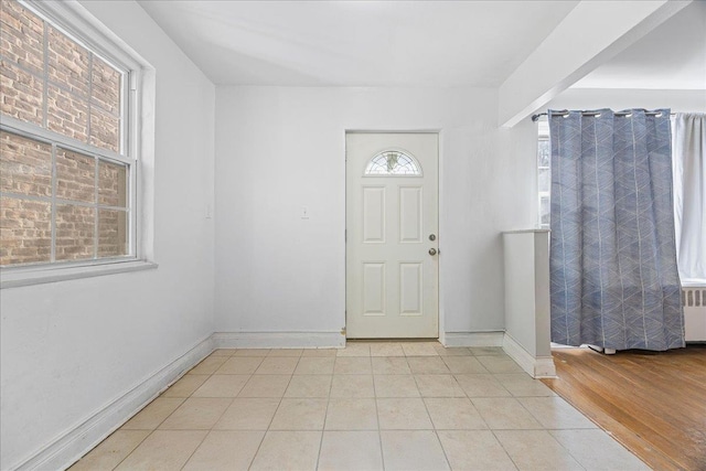 foyer entrance featuring a wealth of natural light, baseboards, radiator, and light tile patterned flooring