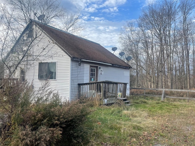 rear view of property featuring fence, roof with shingles, and a deck