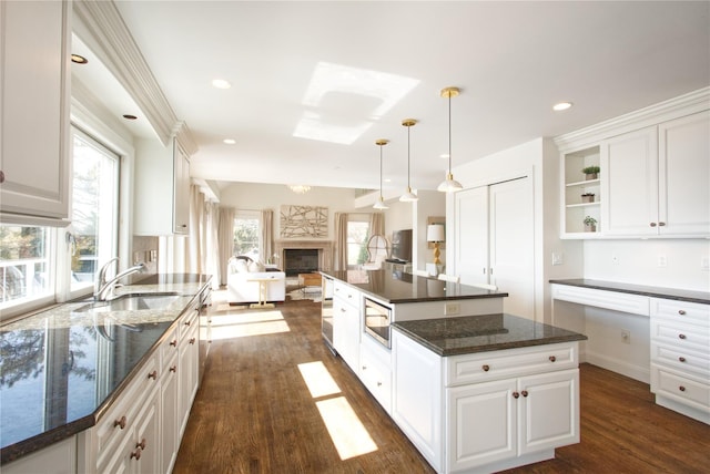 kitchen with open floor plan, white cabinets, a kitchen island, and a sink