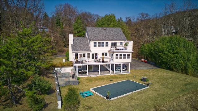 rear view of house with a shingled roof, a chimney, a yard, a balcony, and a patio area