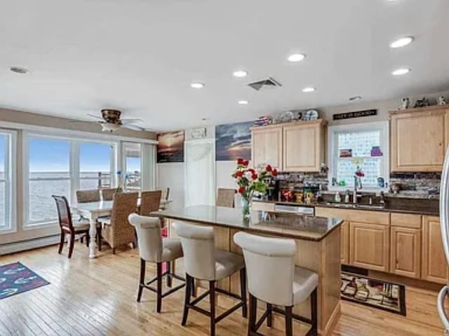 kitchen featuring dark countertops, visible vents, light brown cabinets, a kitchen island, and a breakfast bar