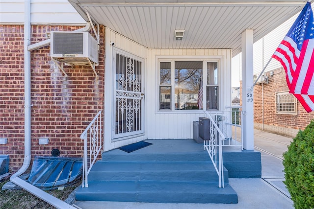 property entrance featuring a wall mounted air conditioner, brick siding, and covered porch