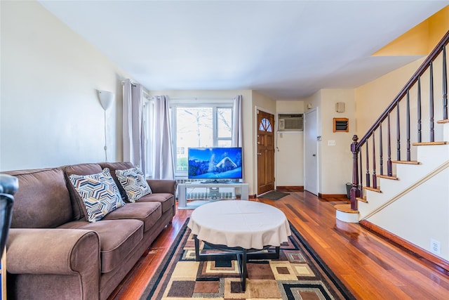 living area featuring a wall unit AC, stairway, wood finished floors, and baseboards