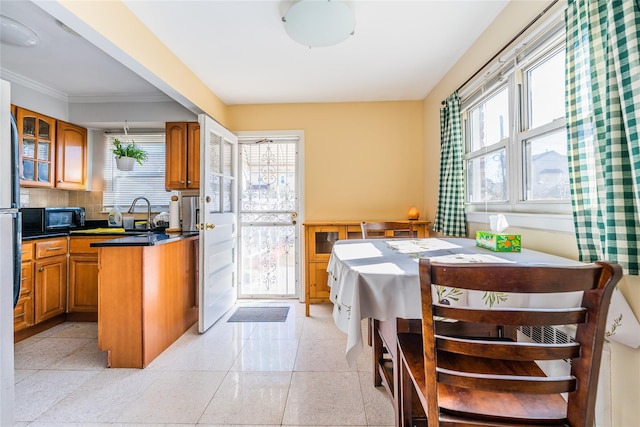 kitchen featuring brown cabinetry, glass insert cabinets, black microwave, dark countertops, and backsplash