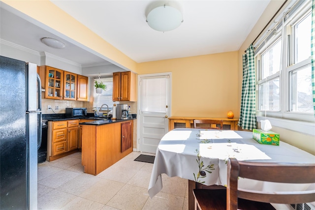 kitchen featuring brown cabinetry, a sink, black appliances, glass insert cabinets, and backsplash