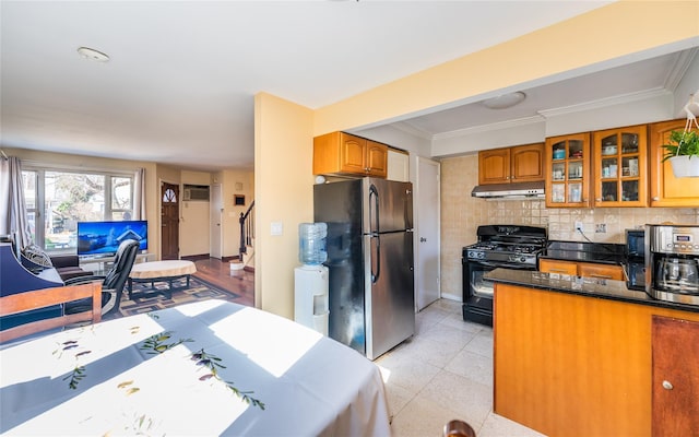 kitchen featuring under cabinet range hood, brown cabinetry, black gas range oven, and freestanding refrigerator