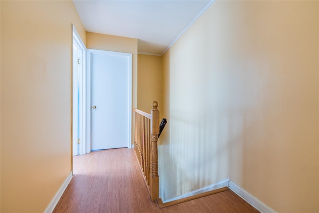 hall featuring an upstairs landing, ornamental molding, baseboards, and wood finished floors