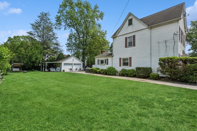 73 Spruce Ave, Floral Park, NY 11001 - view of side of property featuring a detached garage, an outdoor structure, a lawn, and a shingled roof