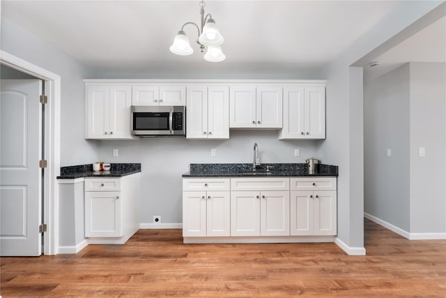 kitchen with stainless steel microwave, white cabinets, light wood-style floors, and a sink