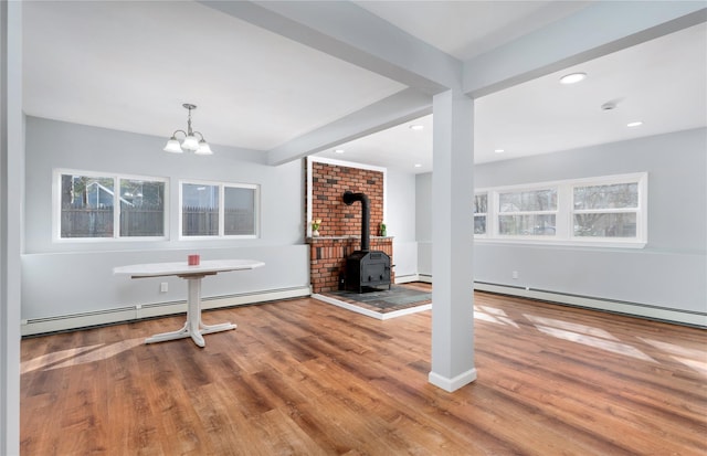 unfurnished living room featuring a baseboard heating unit, beam ceiling, a wood stove, and wood finished floors