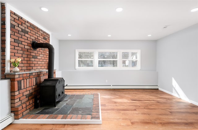 unfurnished living room with recessed lighting, baseboard heating, wood finished floors, and a wood stove