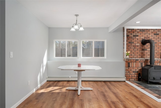 unfurnished dining area featuring wood finished floors, baseboards, a baseboard radiator, a wood stove, and a chandelier