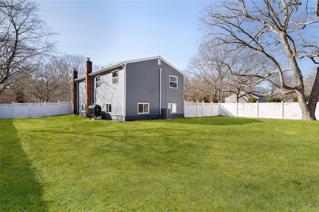 rear view of house with central air condition unit, a lawn, a chimney, and a fenced backyard