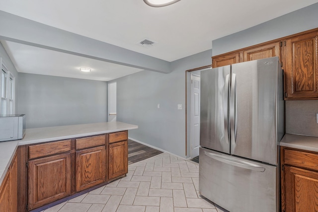 kitchen with visible vents, brown cabinets, white microwave, and freestanding refrigerator