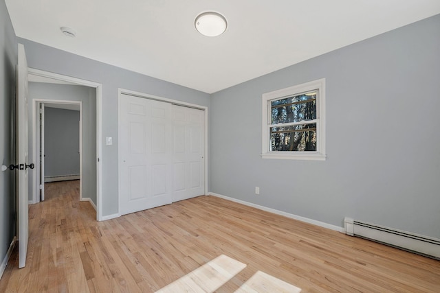 unfurnished bedroom featuring a baseboard heating unit, baseboards, baseboard heating, and light wood-style flooring